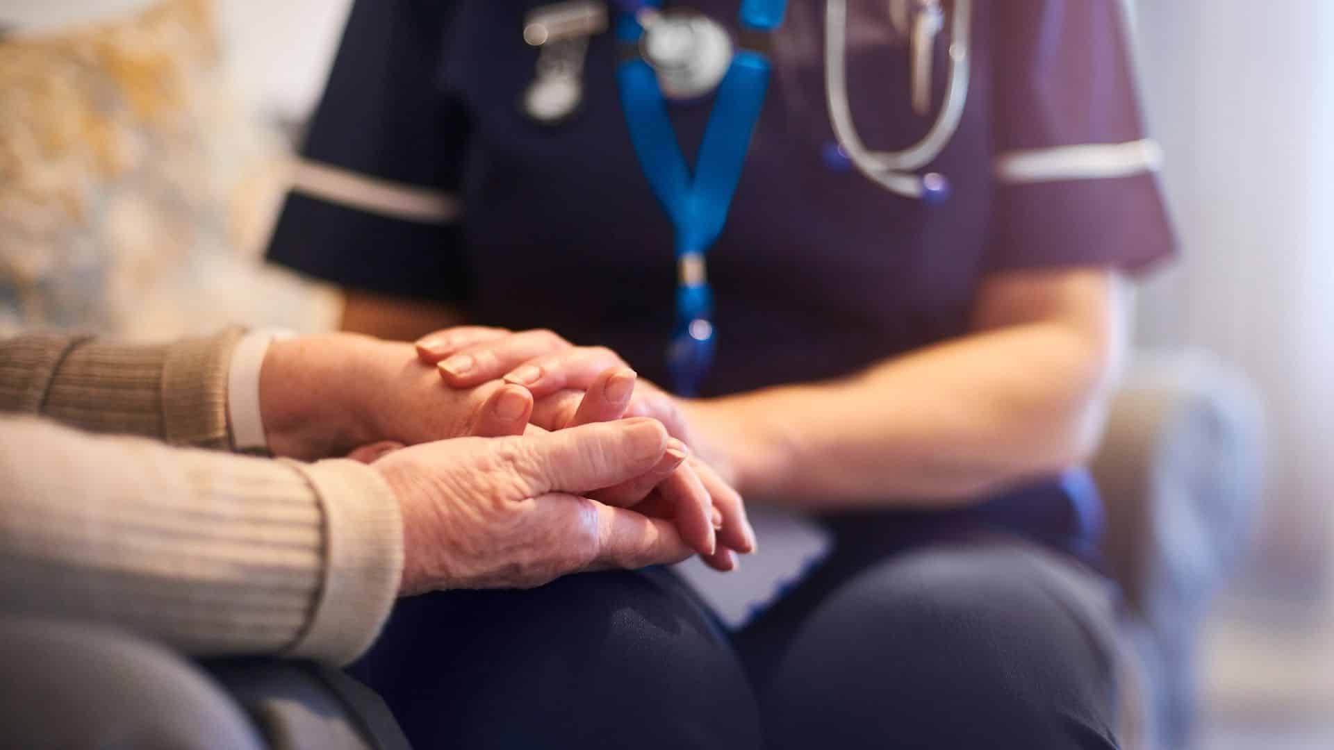 female care professional holding hand of elderly women sitting in a chair