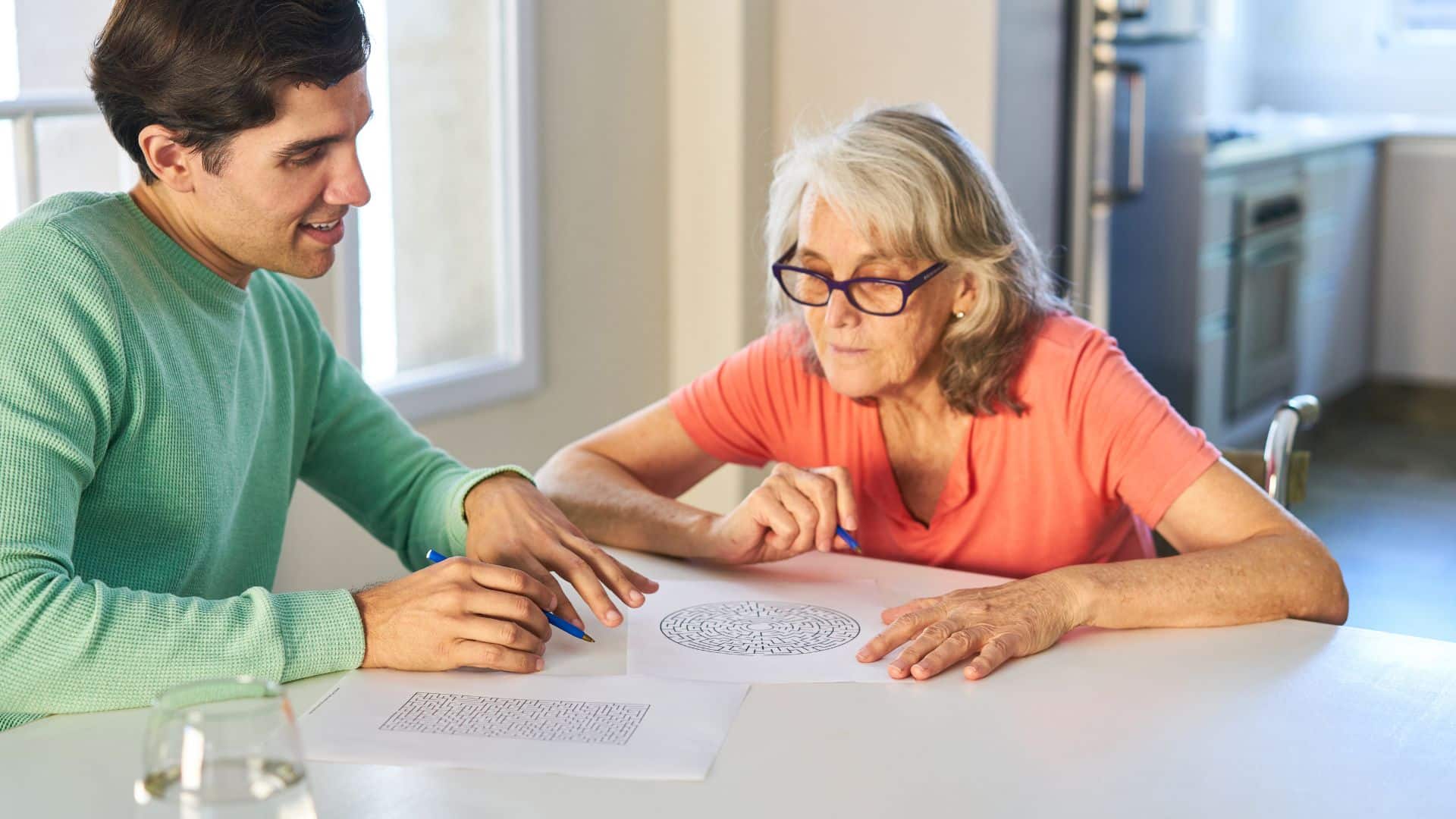 male care professional sitting with elderly women at table doing an activity