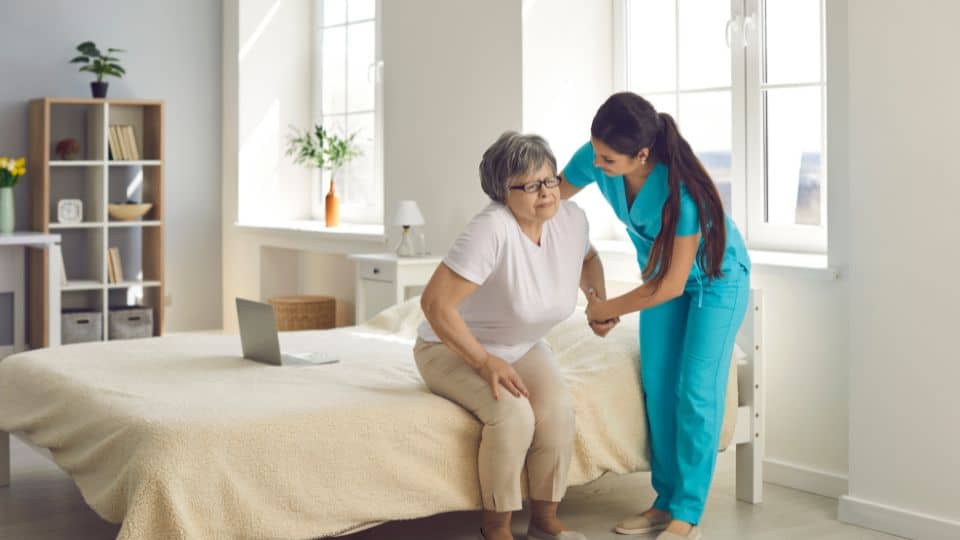 female care professional assisting an elderly women get up off a bed