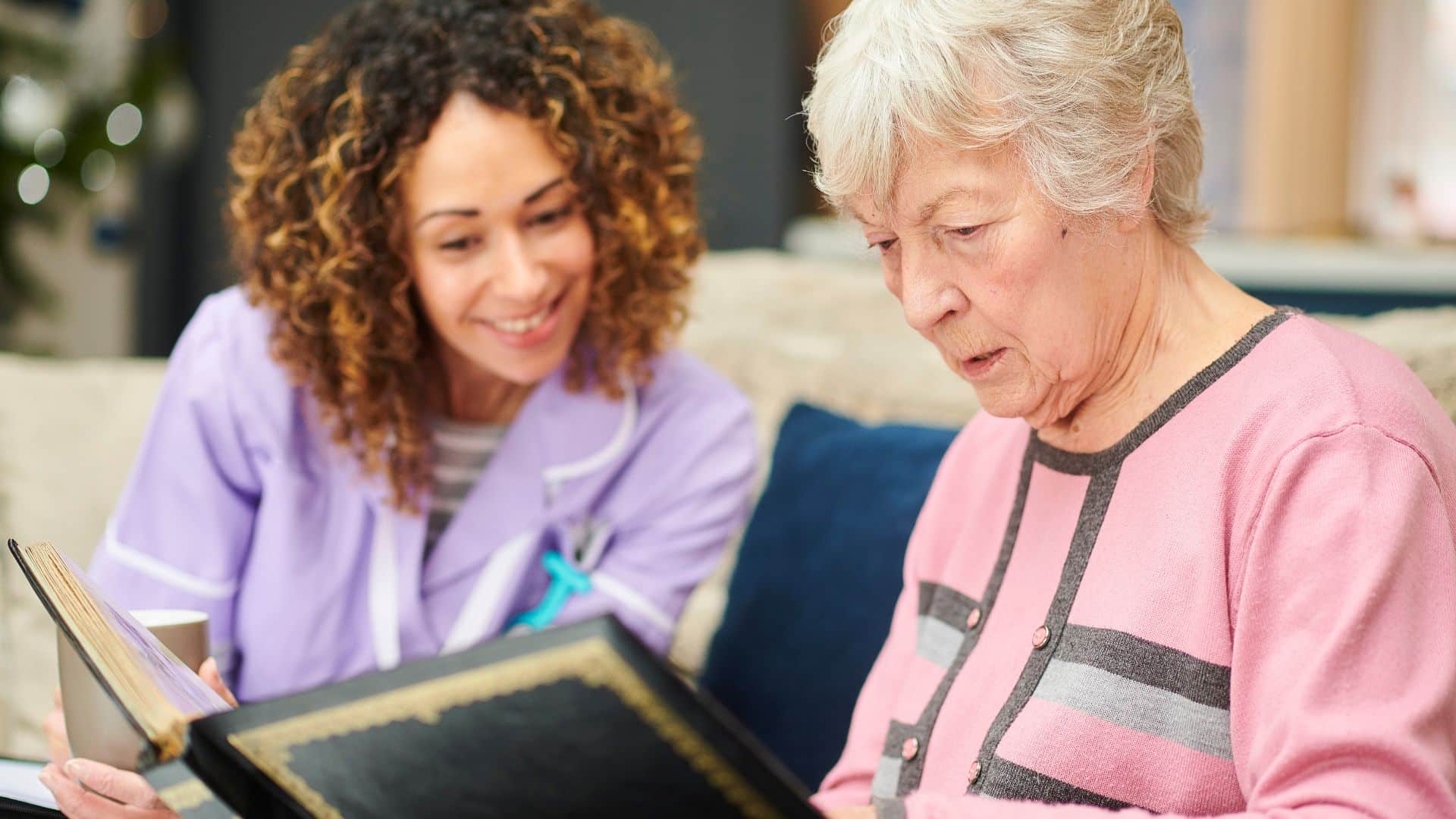 female care professional sitting with elderly lady looking through a photo album