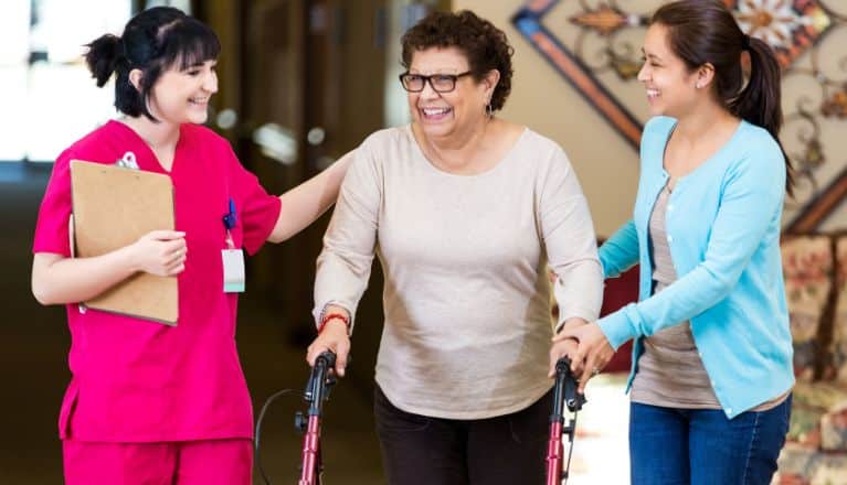 Female Nurse and daughter assisting elderly mother using a mobility aid