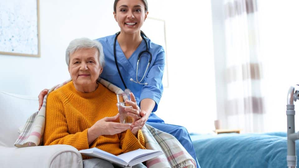 Female care professional sitting next to elderly lady in a chair with a glass of water