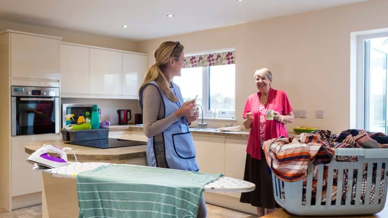 Women at ironing board talking to an elderly women in the kitchen