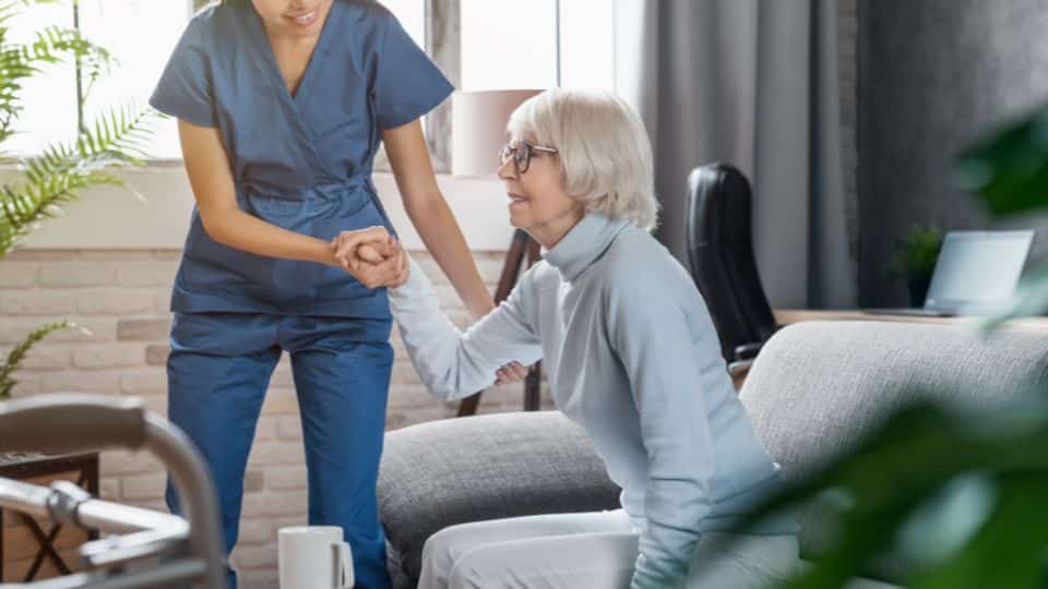 Female care professional assisting an elderly lady get up out of a chair