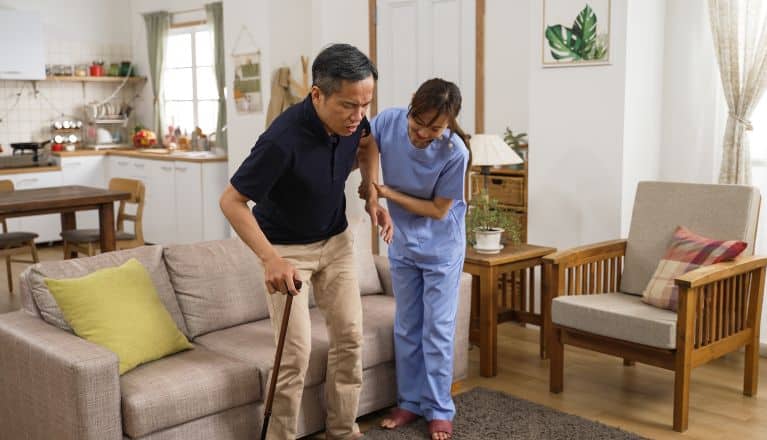 Nurse holding arm of elderly man with walking stick