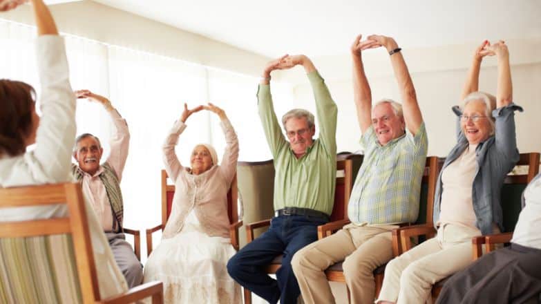 5 older people sitting on chairs doing exercises