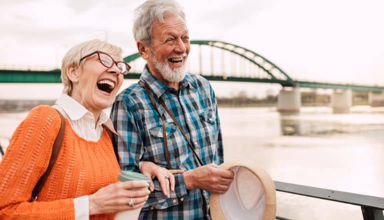 Elderly couple walking and laughing along a river